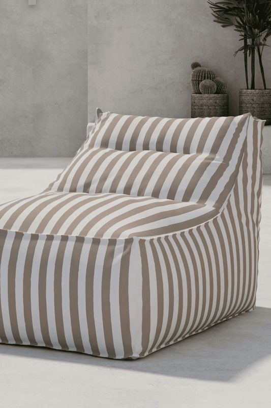 Beige and white striped outdoor bean bag chair with a structured backrest, designed for comfortable lounging in a modern minimalist patio setting featuring concrete flooring and decorative potted plants. | PicSEO 1773145408965