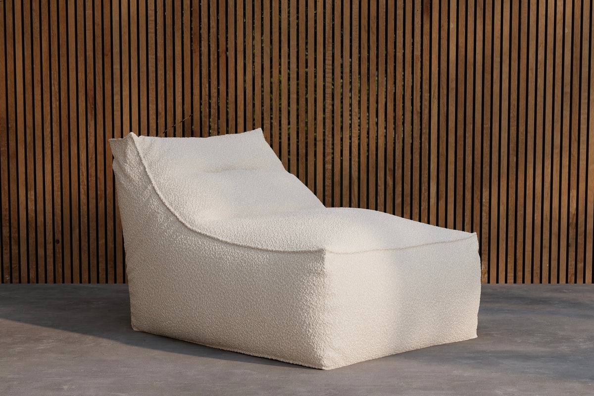Modern off-white textured chaise lounge chair with a minimalist design, set against a vertical wooden slat wall and smooth concrete flooring, ideal for contemporary indoor or outdoor relaxation spaces. | PicSEO 1773145280467