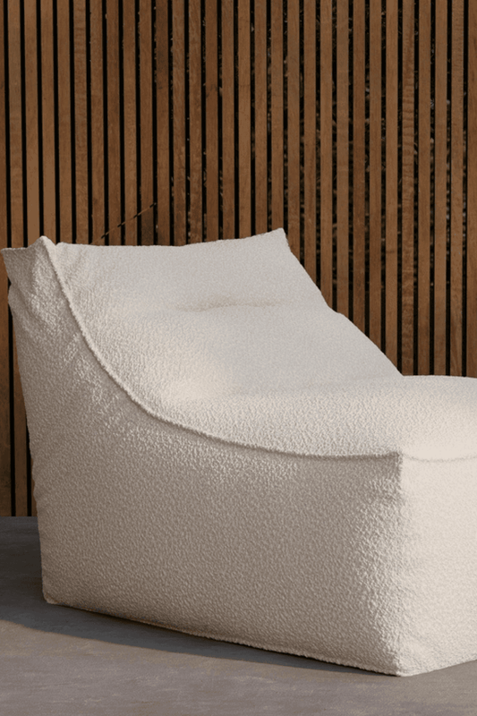 Modern white boucle lounge chair with a soft, textured fabric and minimalist design, placed against a wooden slat wall backdrop. The chair offers comfortable, ergonomic seating with a plush, tufted cushion and a relaxed, low-profile silhouette, ideal for contemporary interiors. | PicSEO 1773145249185