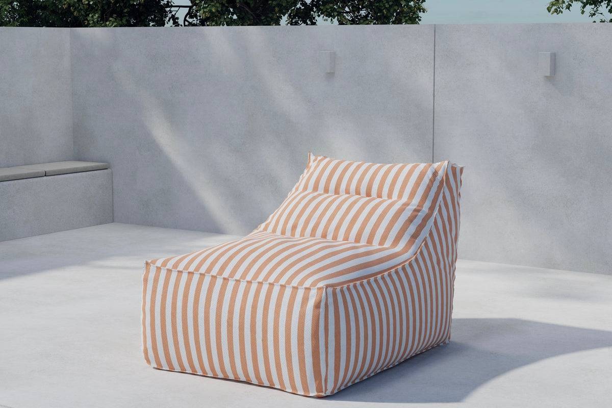 Modern outdoor bean bag chair featuring soft orange and white stripes, designed for comfortable lounging on patios or terraces, set against a minimalistic concrete backdrop with natural sunlight and greenery. | PicSEO 1773145615000