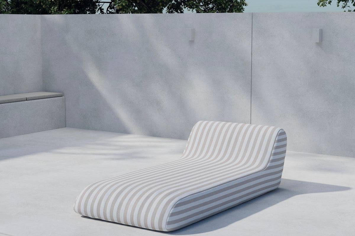 Modern outdoor chaise lounge with a sleek, curved design and beige-and-white striped fabric, set against a minimalist concrete patio and wall, perfect for stylish, comfortable relaxation in an urban garden or terrace. | PicSEO 1773145060212