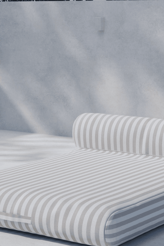 Minimalist outdoor daybed with a cushioned roll pillow, featuring light gray and white vertical stripes, set against a soft gray textured wall, perfect for modern patio or poolside relaxation. | PicSEO 1773144957744