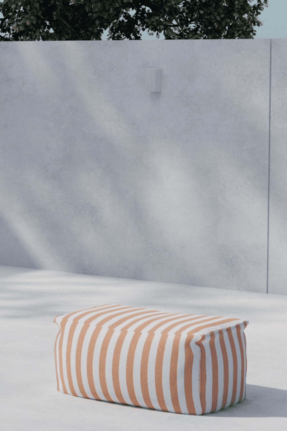 A modern outdoor setting featuring a rectangular pouf with bold orange and white stripes, placed on a smooth concrete surface against a minimalist gray concrete wall with subtle shadows and a hint of greenery above. | PicSEO 1773145199421