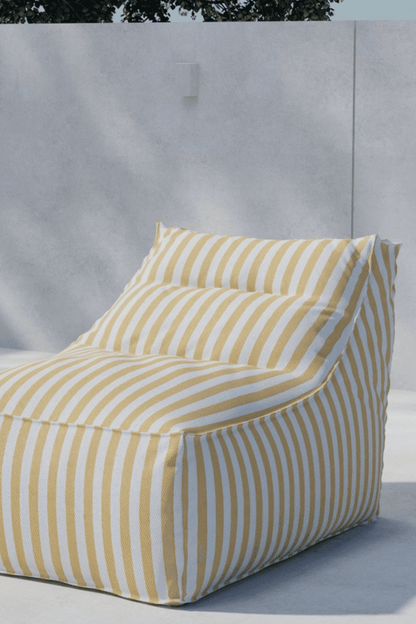Comfortable outdoor bean bag chair with yellow and white vertical stripes, positioned against a minimalist concrete wall in a sunlit patio setting. | PicSEO 1773145541543