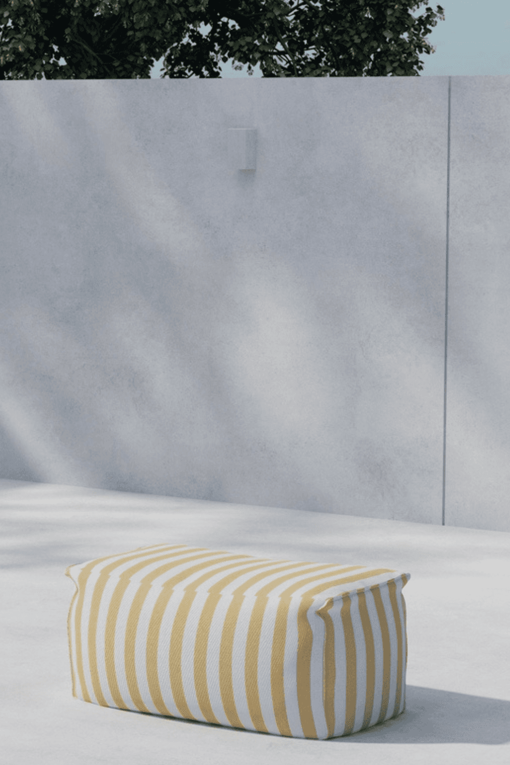 A modern outdoor setting featuring a yellow and white striped rectangular pouf placed on a smooth, light-colored concrete floor, against a minimalist grey wall with subtle shadows and green foliage visible above. | PicSEO 1773145493205